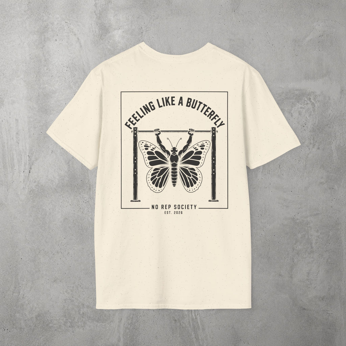 Natural Feeling Like A Butterfly Tee by The No Rep Society, flat lay on grey concrete, back print of a moth with spread wings hanging between two rig uprights under FEELING LIKE A BUTTERFLY lettering.