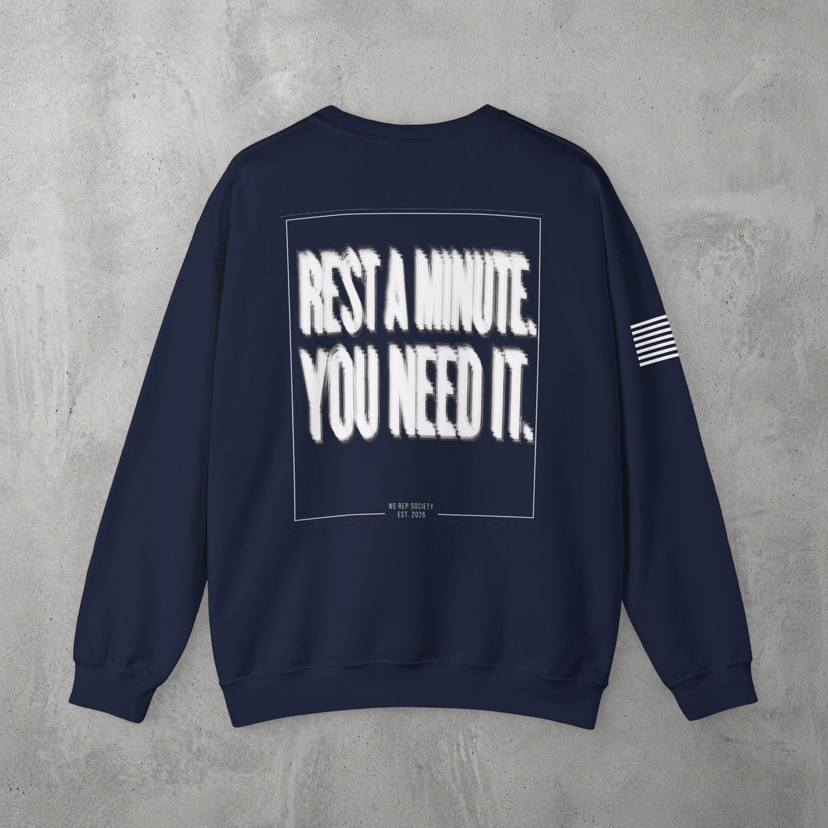 Navy Rest A Minute Crewneck by The No Rep Society, flat lay on grey concrete, back print of REST A MINUTE. YOU NEED IT. in bold blurred capitals inside a thin frame.