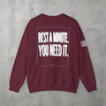 Maroon Rest A Minute Crewneck by The No Rep Society, flat lay on grey concrete, back print of REST A MINUTE. YOU NEED IT. in bold blurred capitals inside a thin frame.