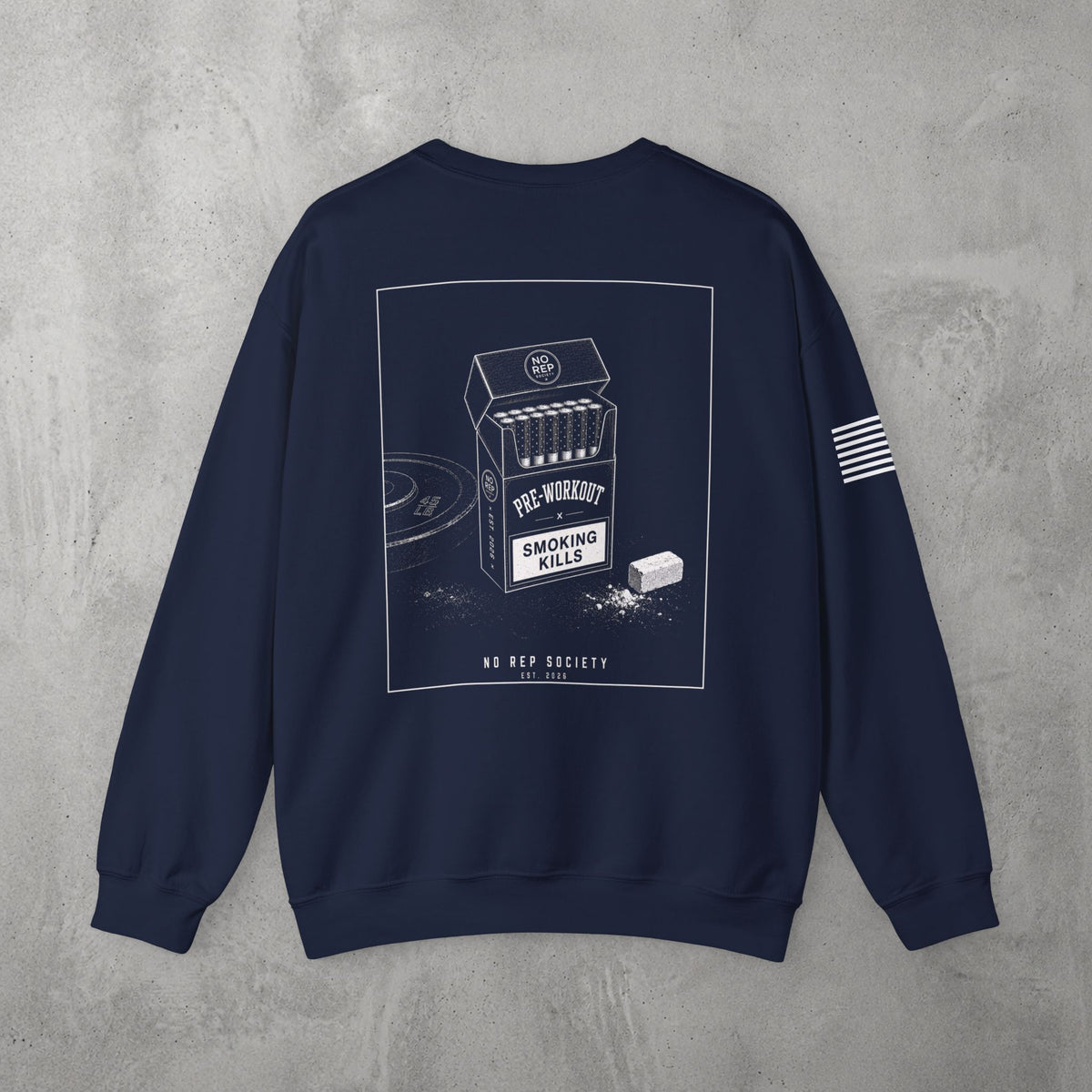 Navy Pre-Workout Crewneck by The No Rep Society, flat lay on grey concrete, back print of an open cigarette pack labelled PRE-WORKOUT with a SMOKING KILLS warning and a scoop spilling powder.