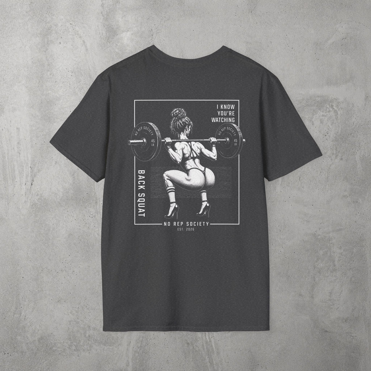 Dark Heather I Know You're Watching Tee by The No Rep Society, flat lay on grey concrete, back print of a woman mid back-squat inside a bordered frame under I KNOW YOU'RE WATCHING lettering.