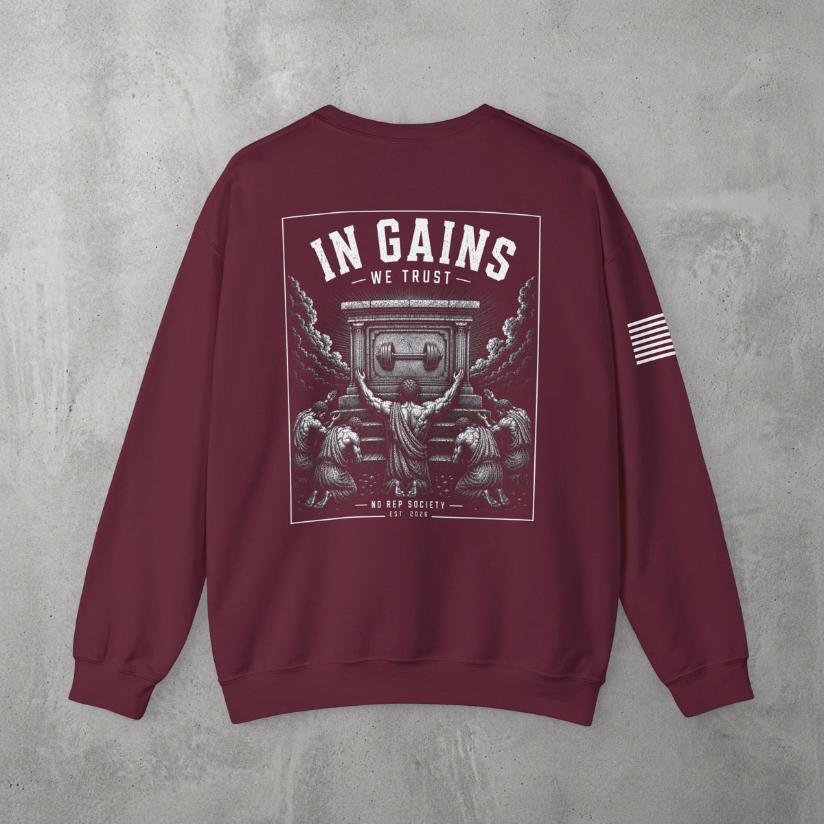 Maroon In Gains We Trust Crewneck by The No Rep Society, flat lay on grey concrete, back print of an ornate temple facade with two kneeling figures and laurel branches under IN GAINS WE TRUST lettering.