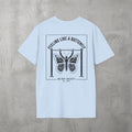 Light Blue Feeling Like A Butterfly Tee by The No Rep Society, flat lay on grey concrete, back print of a moth with spread wings hanging between two rig uprights under FEELING LIKE A BUTTERFLY lettering.