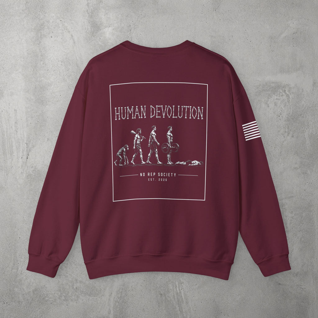 Maroon Human Devolution (MEN) Crewneck by The No Rep Society, flat lay on grey concrete, back print of evolution-of-man silhouettes ending face-down on the floor under HUMAN DEVOLUTION lettering.