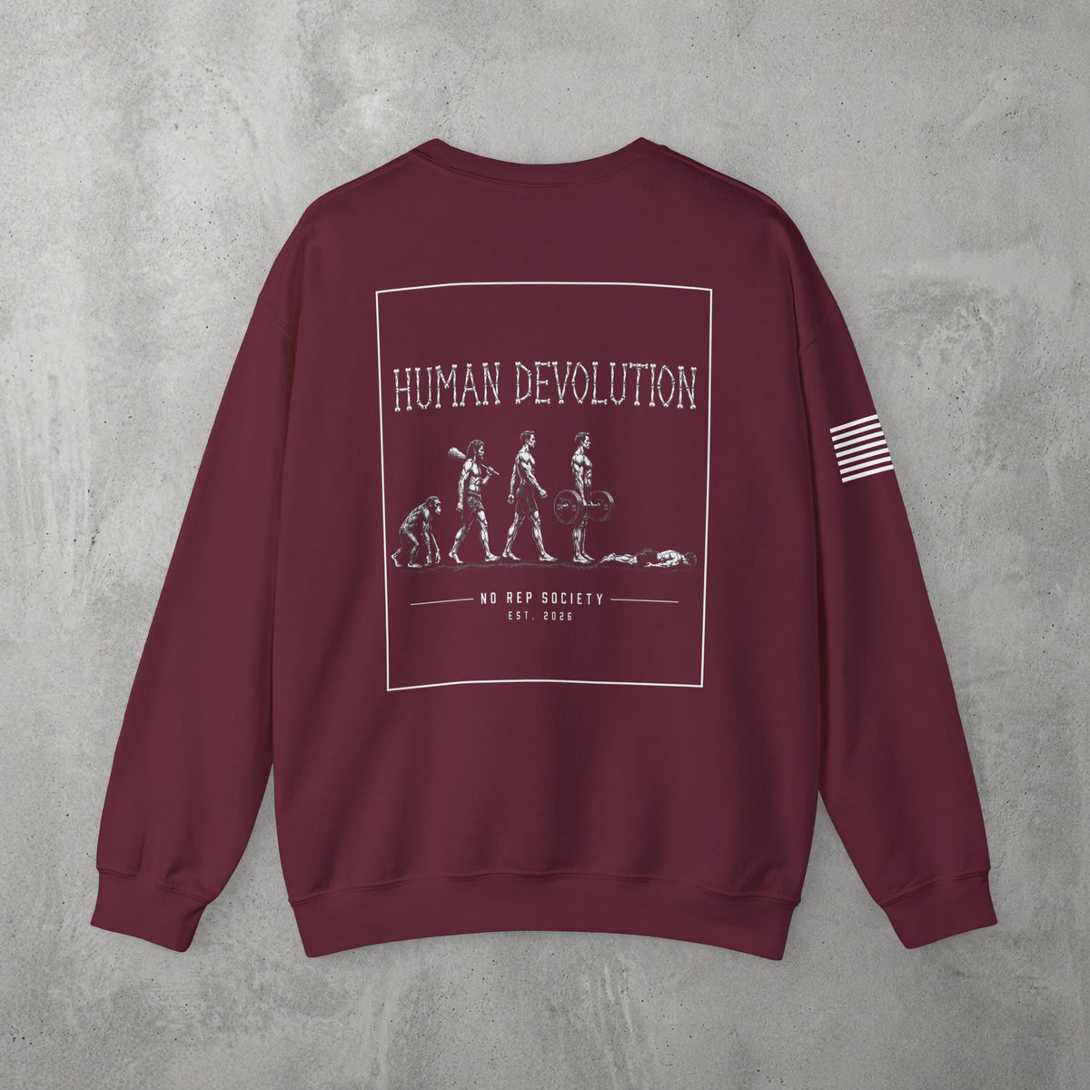 Maroon Human Devolution (MEN) Crewneck by The No Rep Society, flat lay on grey concrete, back print of evolution-of-man silhouettes ending face-down on the floor under HUMAN DEVOLUTION lettering.
