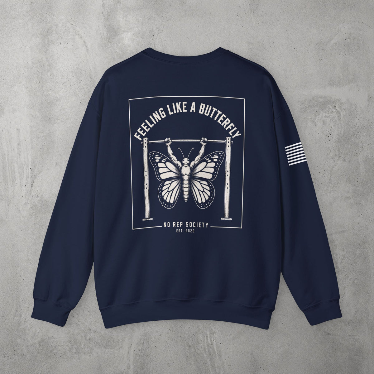 Navy Feeling Like A Butterfly Crewneck by The No Rep Society, flat lay on grey concrete, back print of a moth with spread wings hanging between two rig uprights under FEELING LIKE A BUTTERFLY lettering.