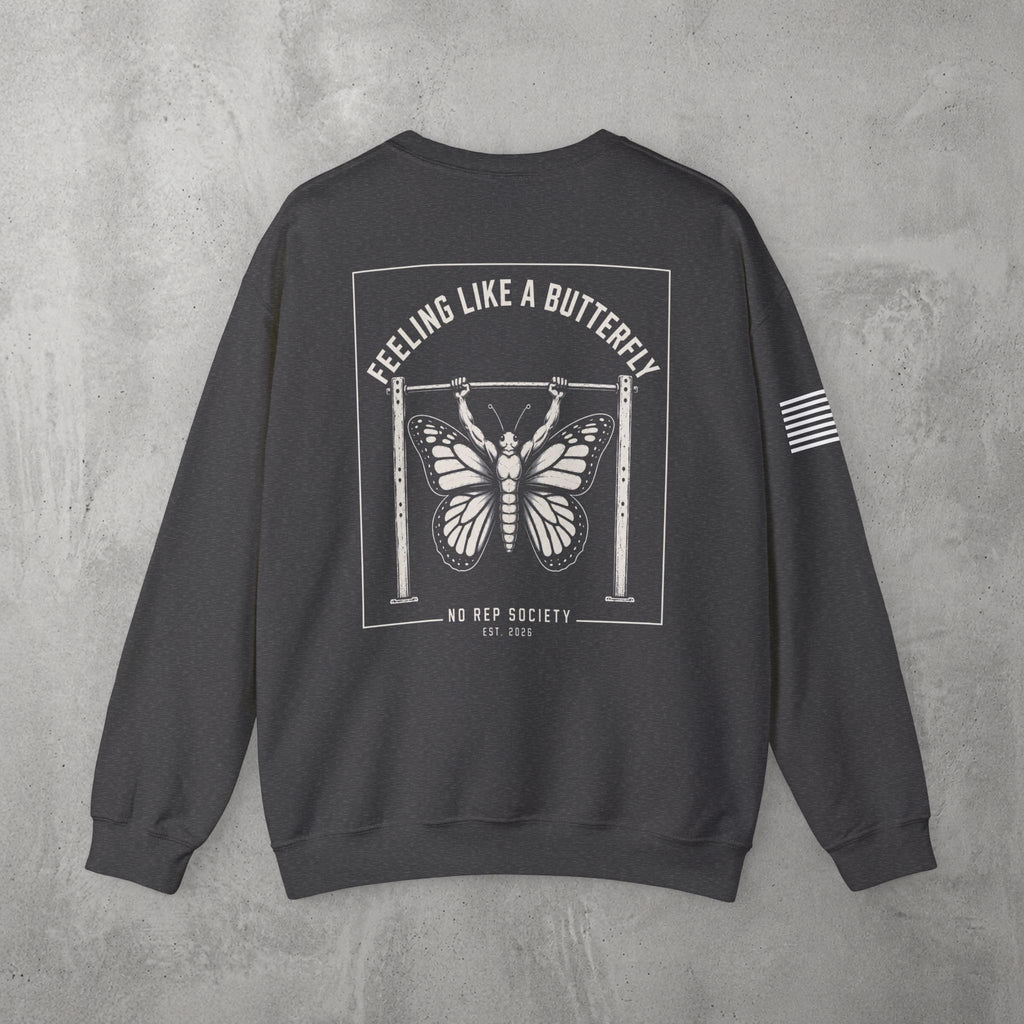 Dark Heather Feeling Like A Butterfly Crewneck by The No Rep Society, flat lay on grey concrete, back print of a moth with spread wings hanging between two rig uprights under FEELING LIKE A BUTTERFLY lettering.