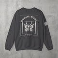 Dark Heather Feeling Like A Butterfly Crewneck by The No Rep Society, flat lay on grey concrete, back print of a moth with spread wings hanging between two rig uprights under FEELING LIKE A BUTTERFLY lettering.