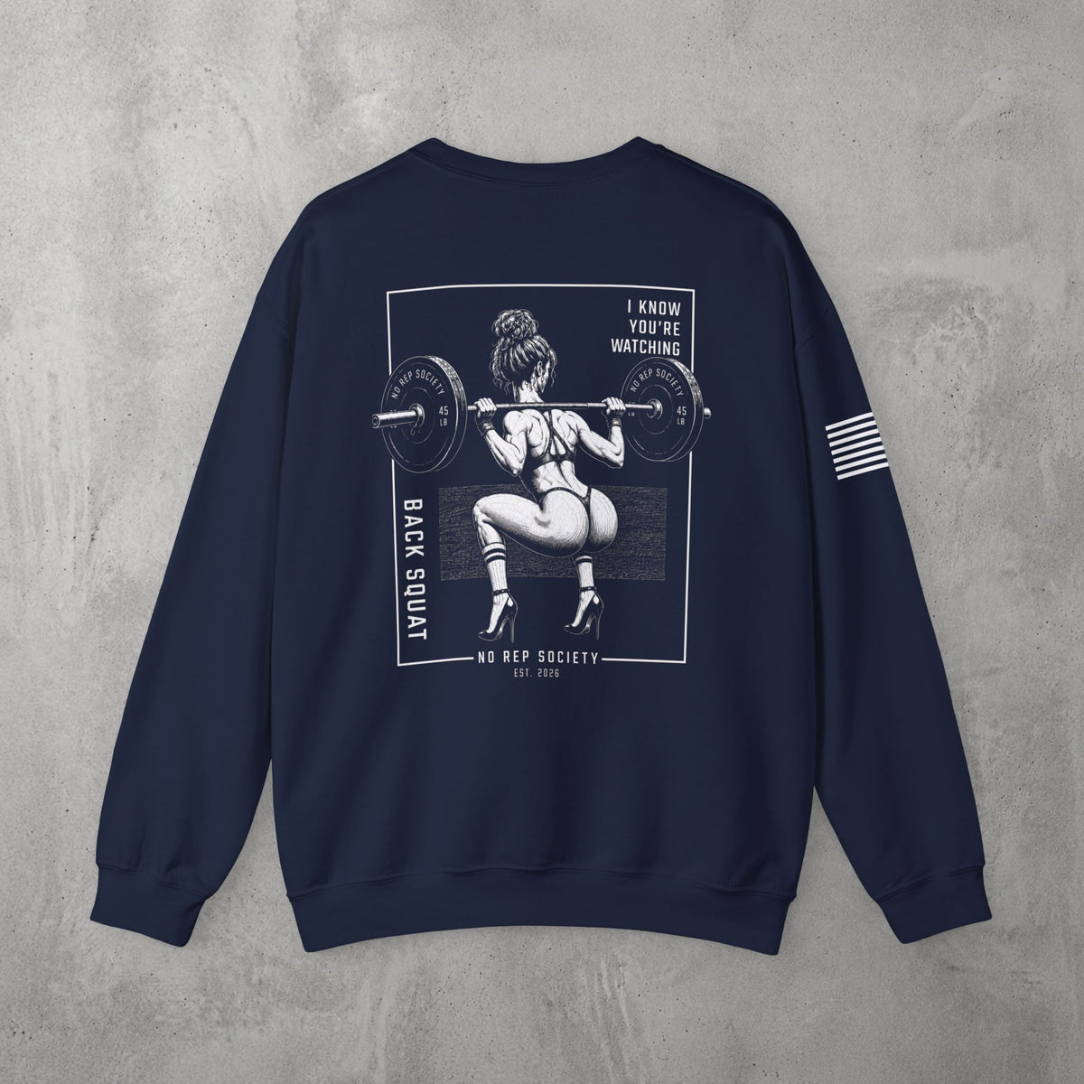Navy I Know You're Watching Crewneck by The No Rep Society, flat lay on grey concrete, back print of a woman mid back-squat inside a bordered frame under I KNOW YOU'RE WATCHING lettering.