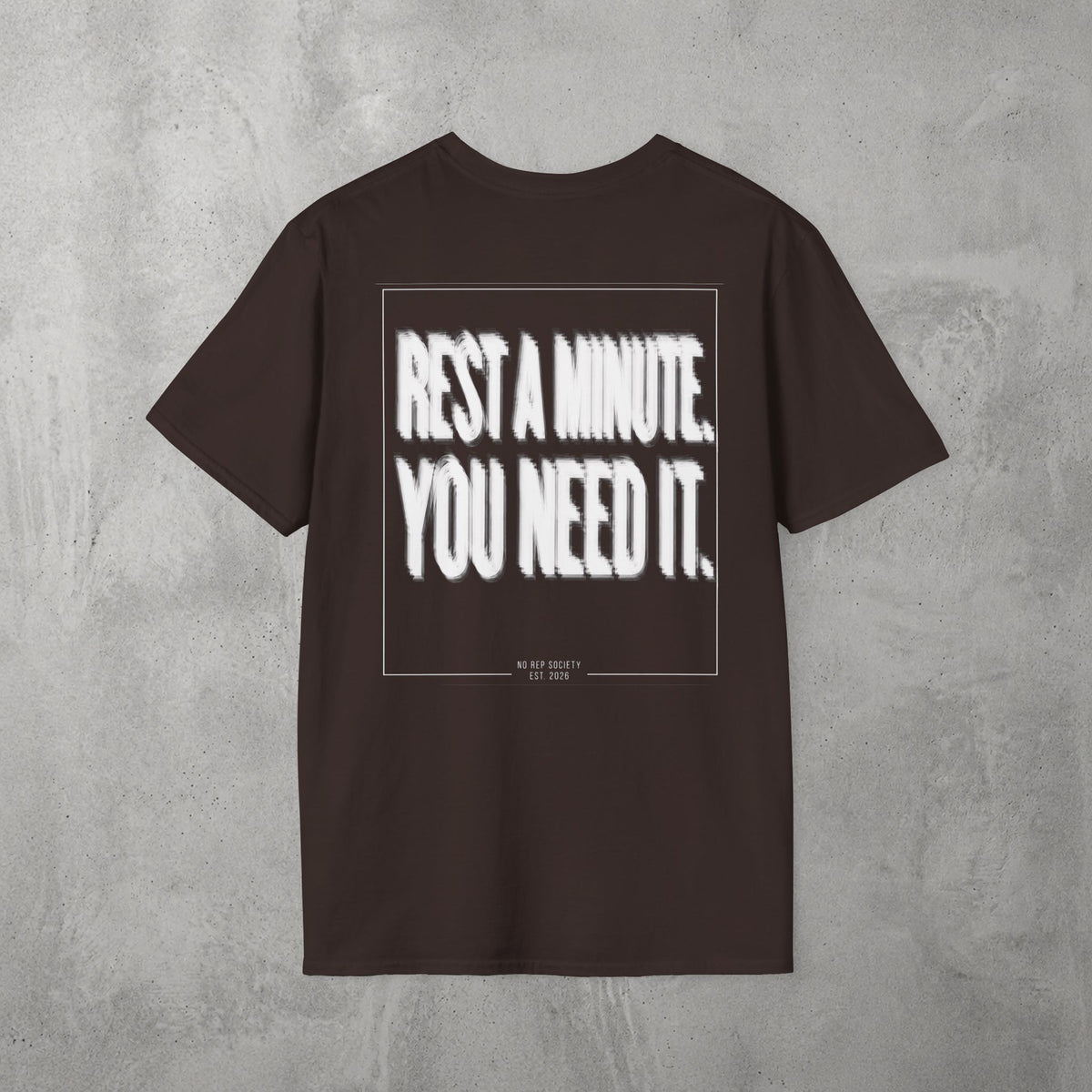 Dark Chocolate Rest A Minute Tee by The No Rep Society, flat lay on grey concrete, back print of REST A MINUTE. YOU NEED IT. in bold blurred capitals inside a thin frame.