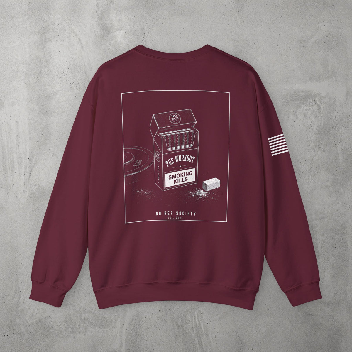 Maroon Pre-Workout Crewneck by The No Rep Society, flat lay on grey concrete, back print of an open cigarette pack labelled PRE-WORKOUT with a SMOKING KILLS warning and a scoop spilling powder.