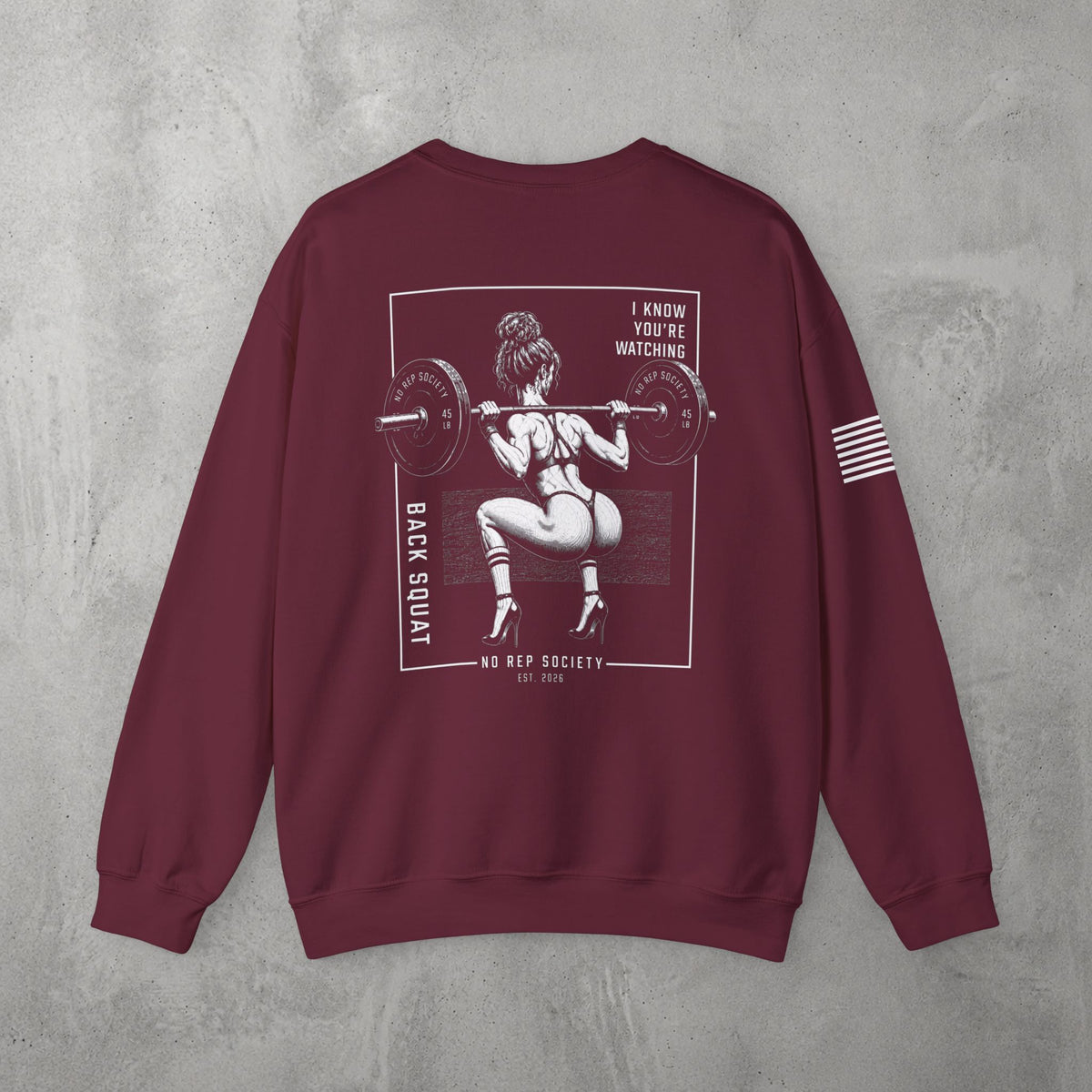 Maroon I Know You're Watching Crewneck by The No Rep Society, flat lay on grey concrete, back print of a woman mid back-squat inside a bordered frame under I KNOW YOU'RE WATCHING lettering.