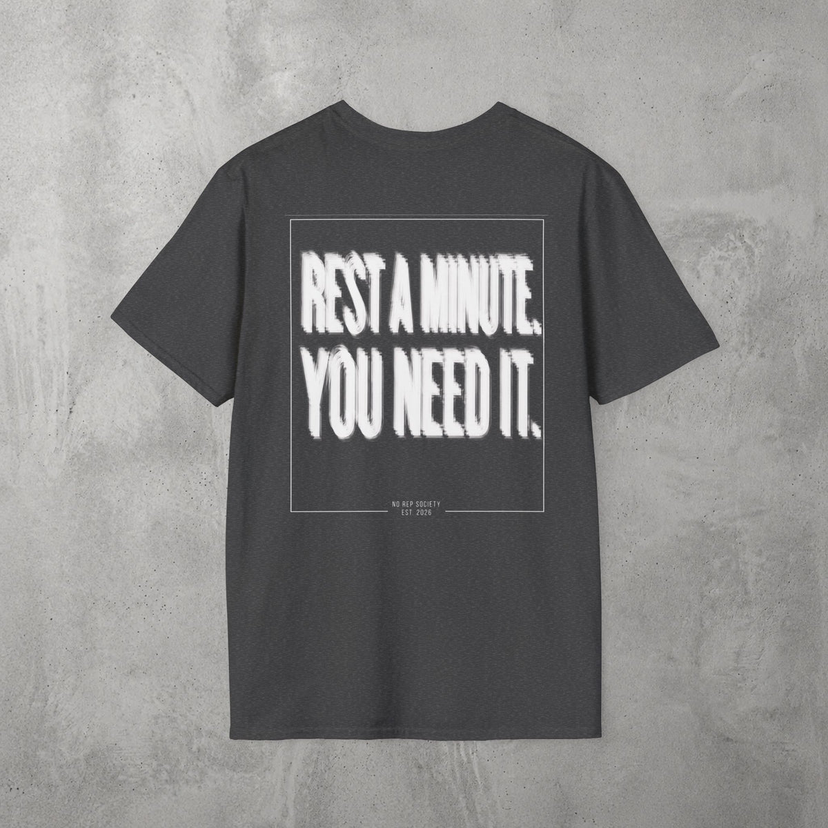 Dark Heather Rest A Minute Tee by The No Rep Society, flat lay on grey concrete, back print of REST A MINUTE. YOU NEED IT. in bold blurred capitals inside a thin frame.