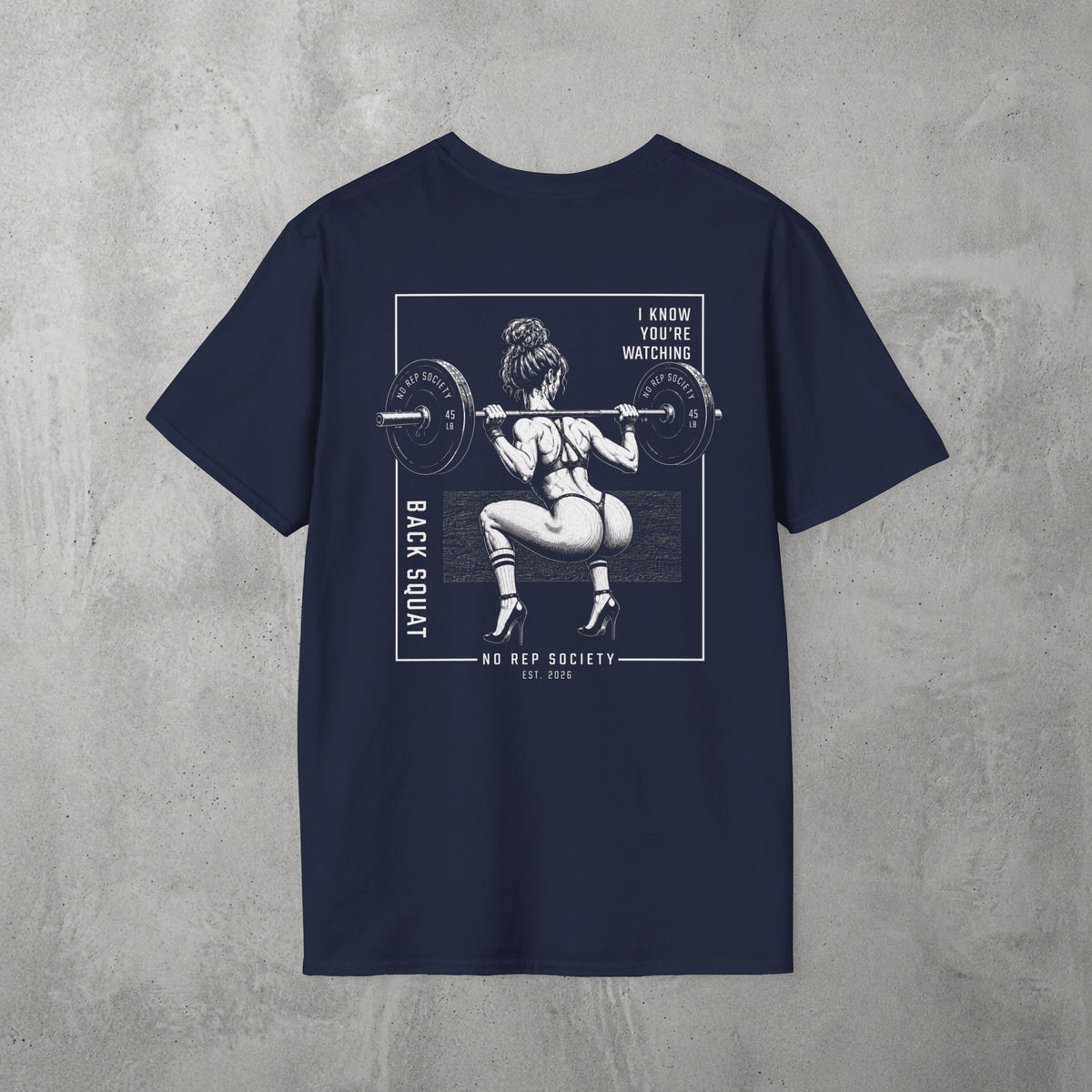 Navy I Know You're Watching Tee by The No Rep Society, flat lay on grey concrete, back print of a woman mid back-squat inside a bordered frame under I KNOW YOU'RE WATCHING lettering.