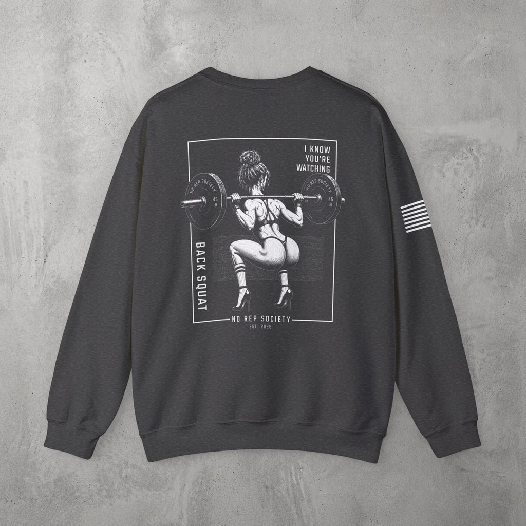 Dark Heather I Know You're Watching Crewneck by The No Rep Society, flat lay on grey concrete, back print of a woman mid back-squat inside a bordered frame under I KNOW YOU'RE WATCHING lettering.