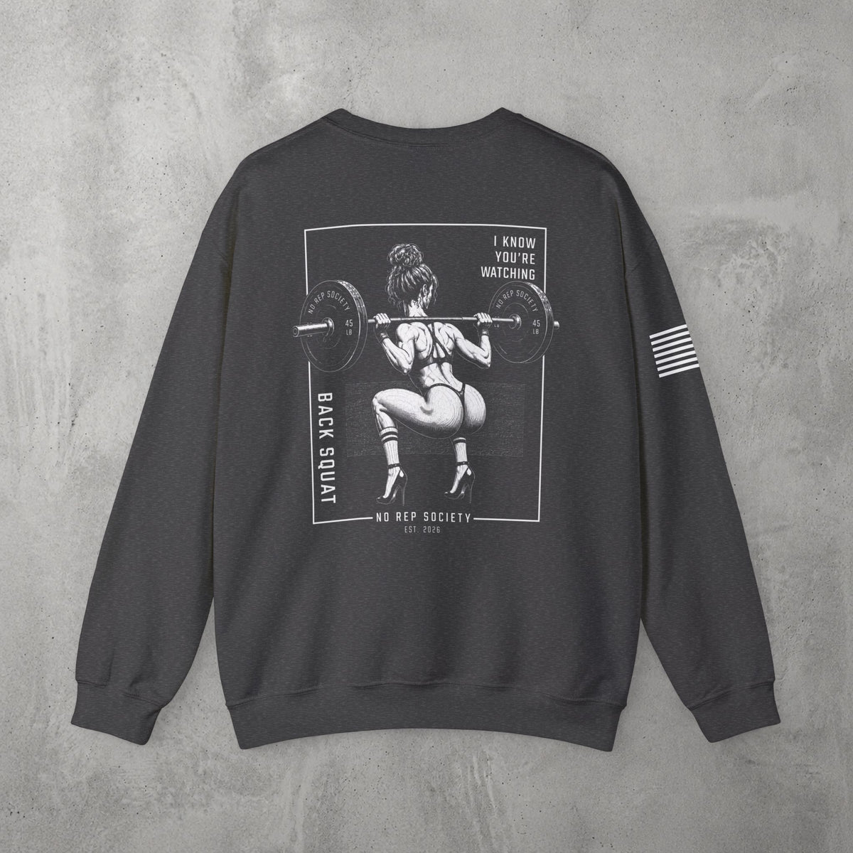 Dark Heather I Know You're Watching Crewneck by The No Rep Society, flat lay on grey concrete, back print of a woman mid back-squat inside a bordered frame under I KNOW YOU'RE WATCHING lettering.