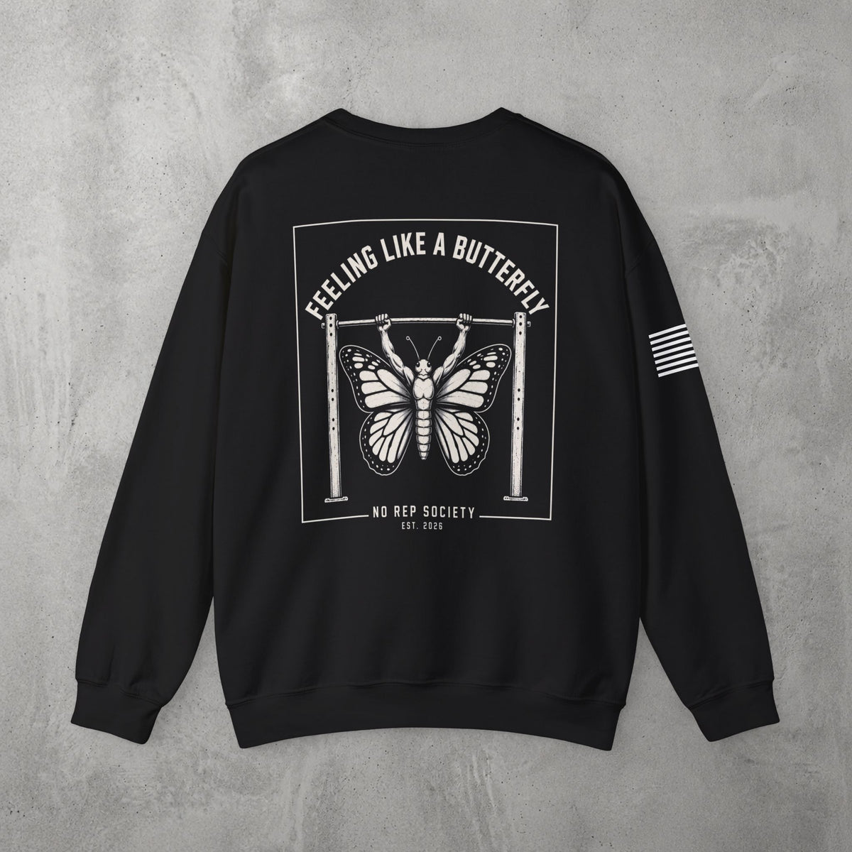 Black Feeling Like A Butterfly Crewneck by The No Rep Society, flat lay on grey concrete, back print of a moth with spread wings hanging between two rig uprights under FEELING LIKE A BUTTERFLY lettering.