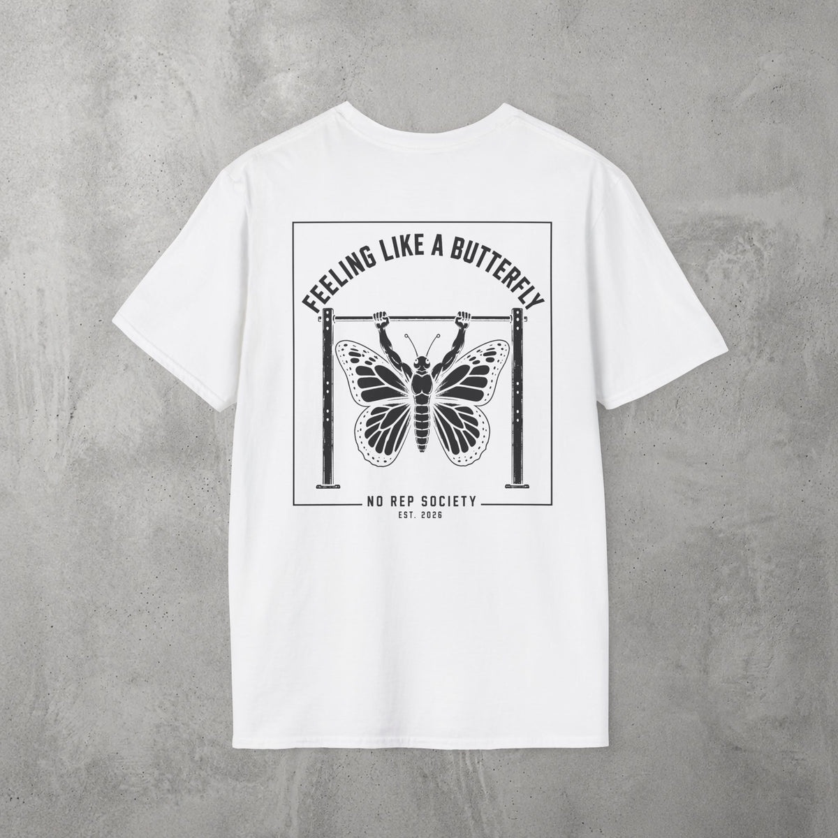 White Feeling Like A Butterfly Tee by The No Rep Society, flat lay on grey concrete, back print of a moth with spread wings hanging between two rig uprights under FEELING LIKE A BUTTERFLY lettering.