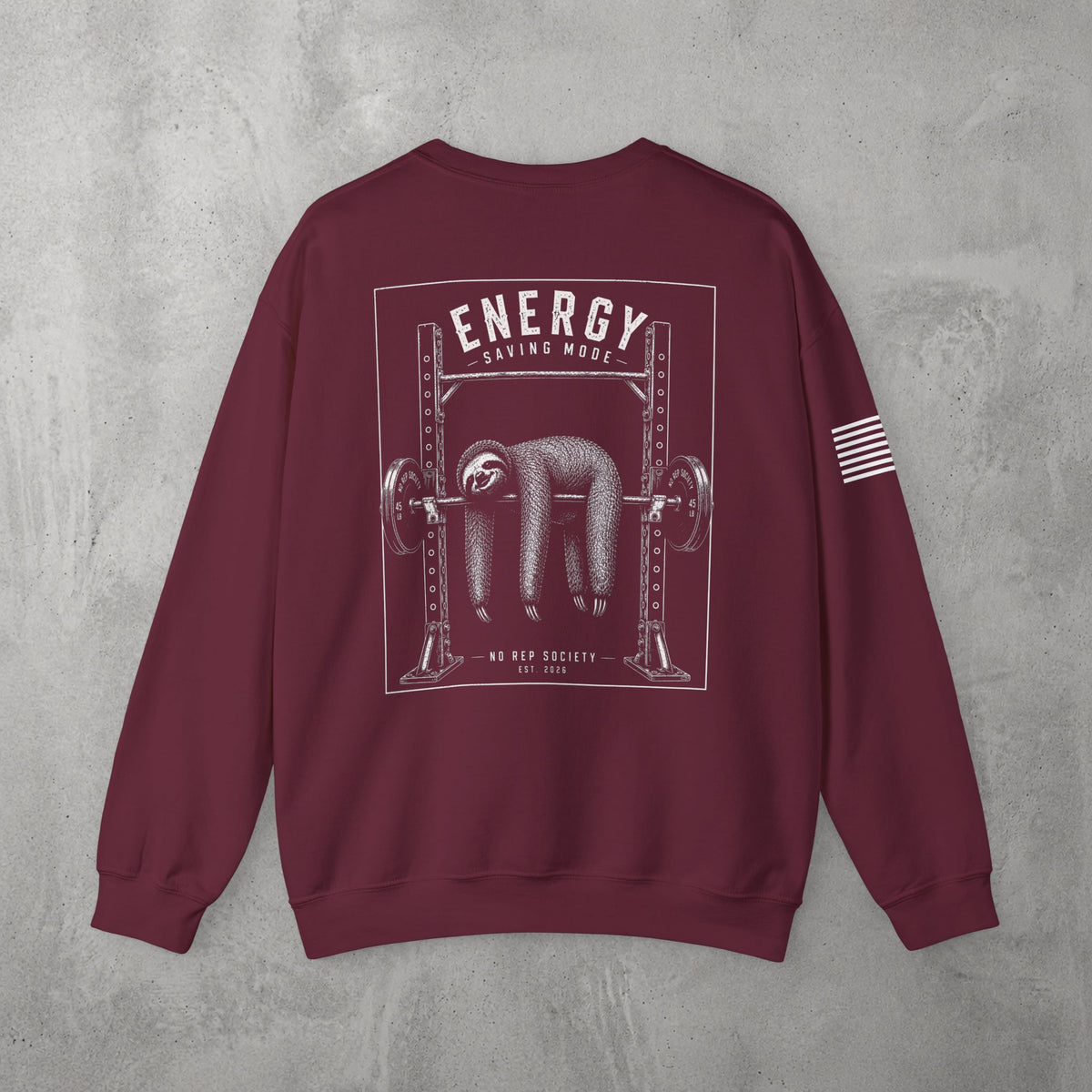 Maroon Energy Saving Mode Crewneck by The No Rep Society, flat lay on grey concrete, back print of a sloth hanging from a loaded barbell in a squat rack under ENERGY SAVING MODE lettering.