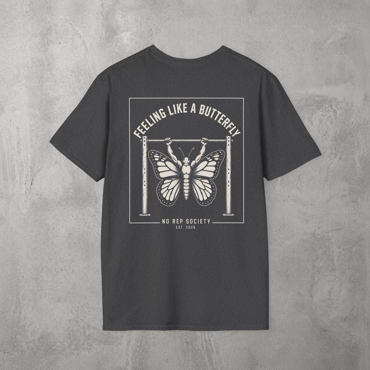 Dark Heather Feeling Like A Butterfly Tee by The No Rep Society, flat lay on grey concrete, back print of a moth with spread wings hanging between two rig uprights under FEELING LIKE A BUTTERFLY lettering.