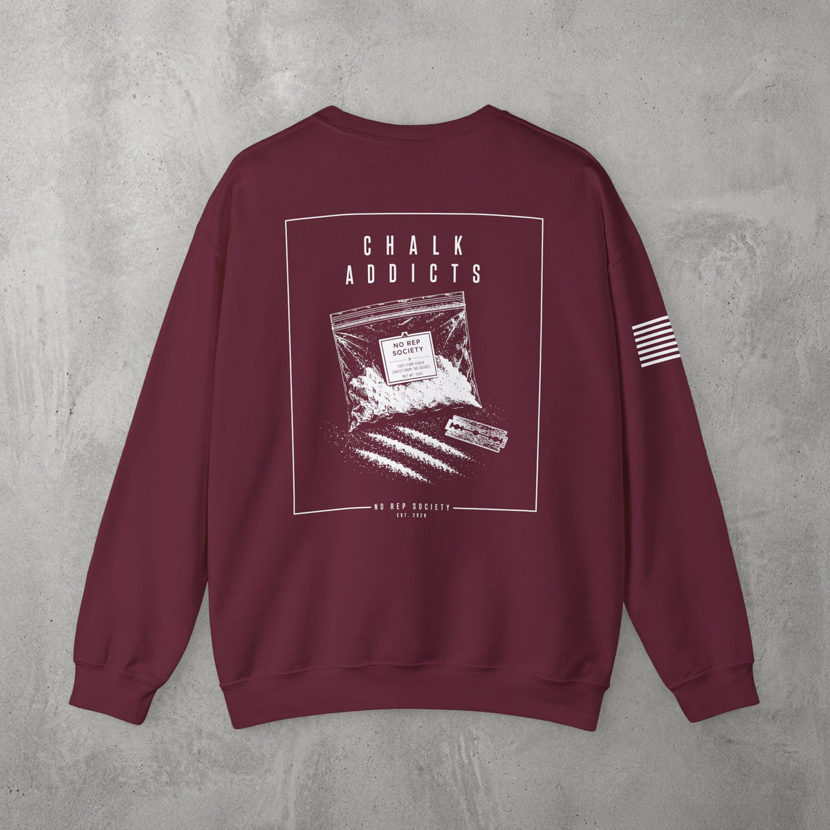 Maroon Chalk Addicts Crewneck by The No Rep Society, flat lay on grey concrete, back print of an open bag of gym chalk spilling across a bordered frame under CHALK ADDICTS lettering.