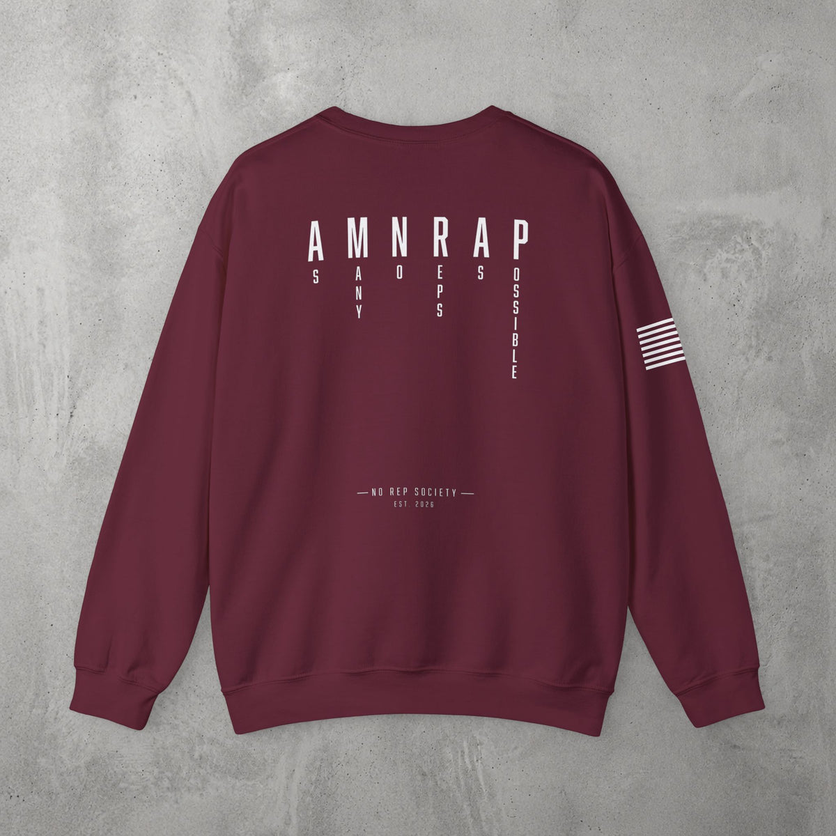 Maroon AMNRAP Crewneck by The No Rep Society, flat lay on grey concrete, back print of AMNRAP in wide spaced capitals with AS MANY NO-REPS AS POSSIBLE set vertically between the letters.