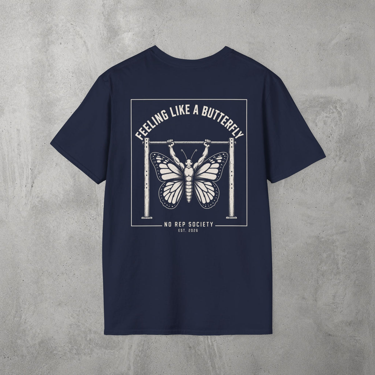 Navy Feeling Like A Butterfly Tee by The No Rep Society, flat lay on grey concrete, back print of a moth with spread wings hanging between two rig uprights under FEELING LIKE A BUTTERFLY lettering.