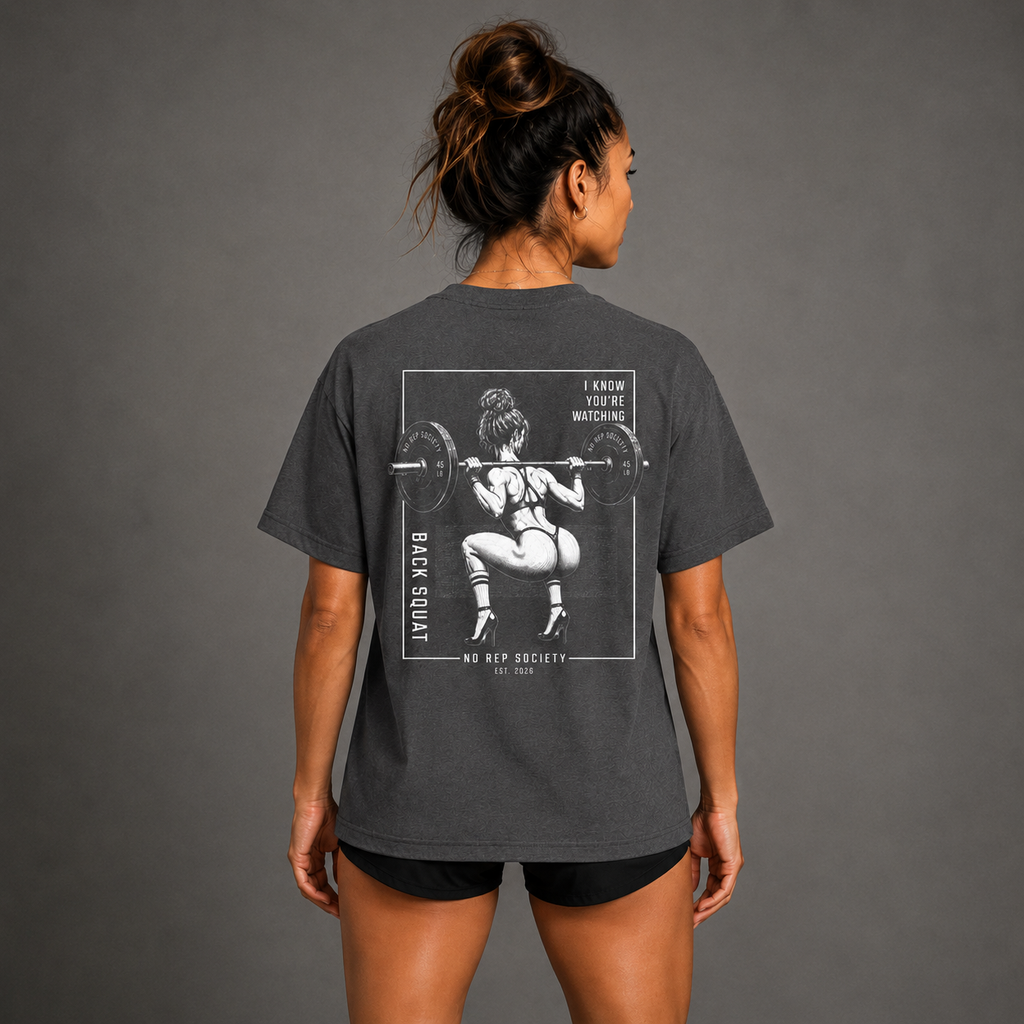 Dark Heather I Know You're Watching Tee by The No Rep Society, worn by a female model, back view showing the I KNOW YOU'RE WATCHING print.